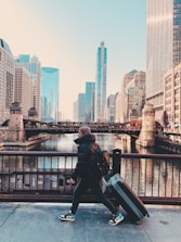 man in black jacket sitting on black metal railings near body of water during daytime