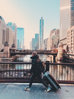man in black jacket sitting on black metal railings near body of water during daytime