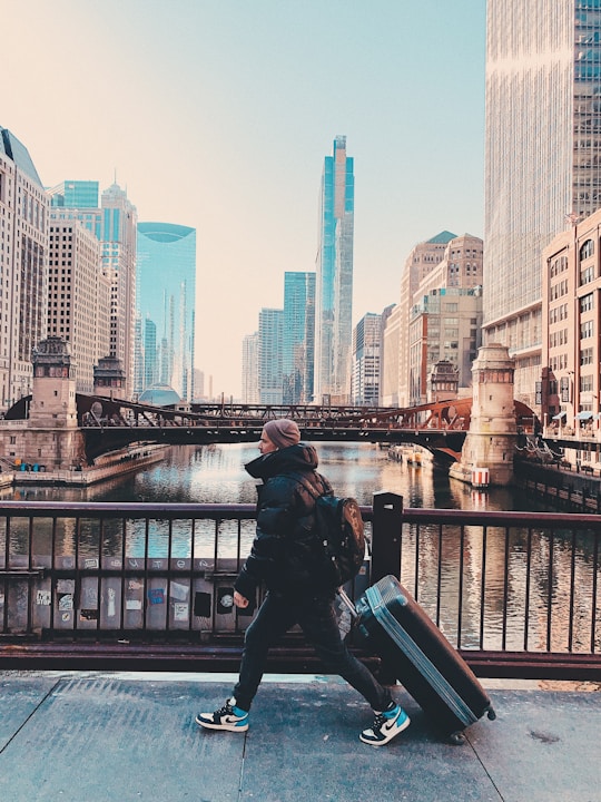 man in black jacket sitting on black metal railings near body of water during daytime