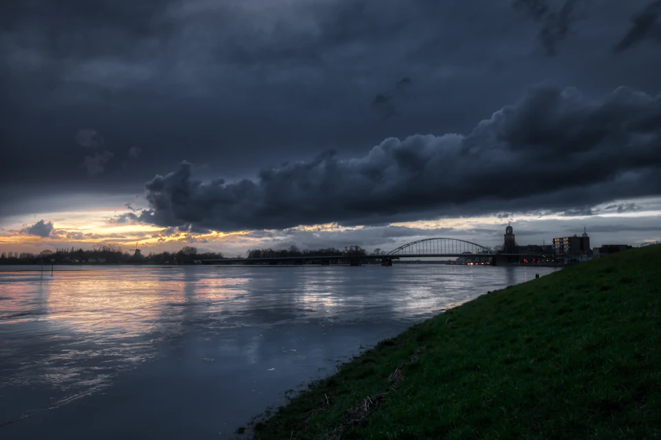 Serene river scene at sunset with a bridge spanning across it and surrounding landscape
