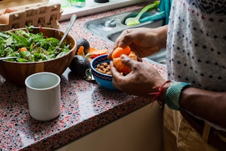 person holding orange fruit on blue ceramic bowl