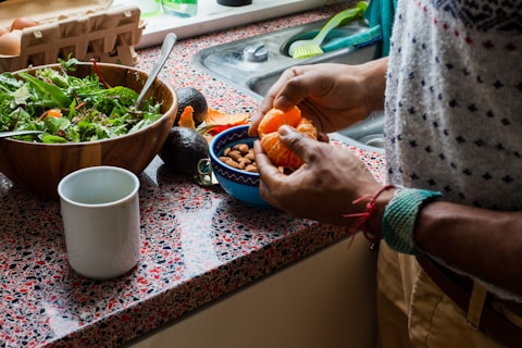 person holding orange fruit on blue ceramic bowl