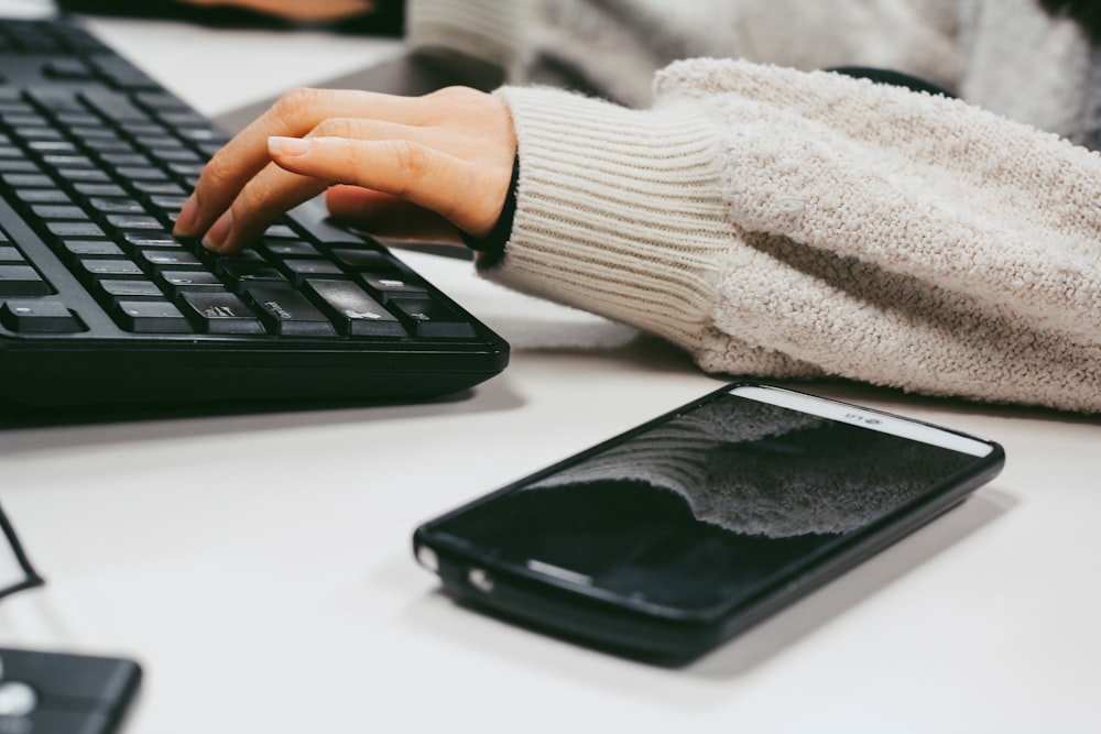 person in white sweater holding black smartphone