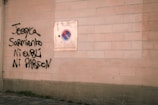 Graffiti in black spray paint is visible beneath a no-parking sign mounted on a light brick wall. The graffiti contains names and a phrase written in French.