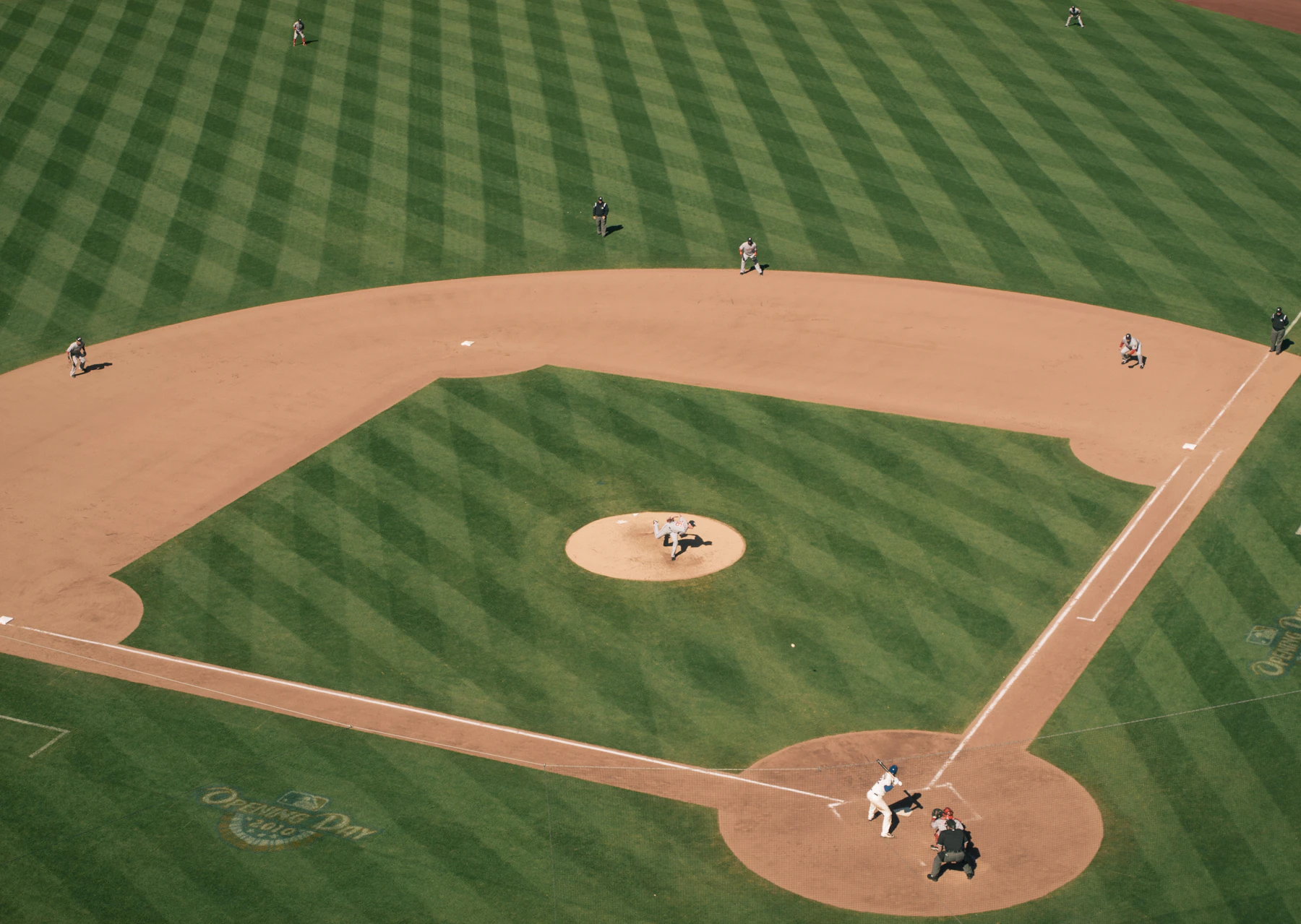 A baseball infield seen from above: striped grass, a pitcher on the mound and a batter at home plate