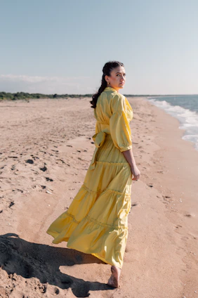 Sunlit California beach scene with a stylish woman walking along the shore, embodying effortless chic.