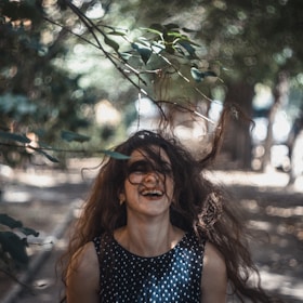 A candid photo of a woman laughing freely in a sunlit park, surrounded by blooming flowers.