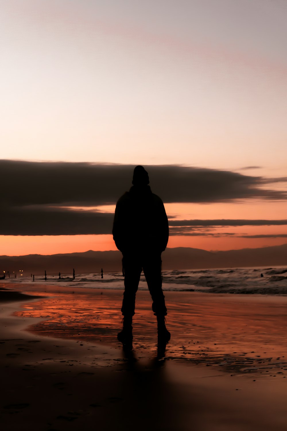 silhueta do homem em pé na praia durante o pôr do sol