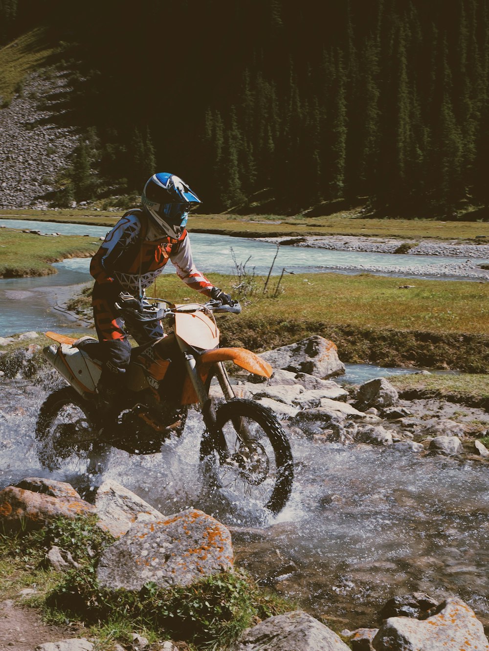 man riding orange and black motorcycle on river during daytime