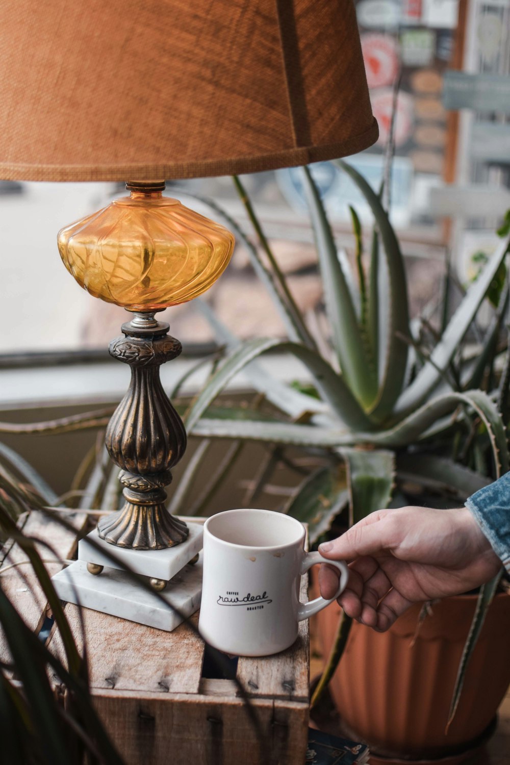 person holding white ceramic mug near brown table lamp