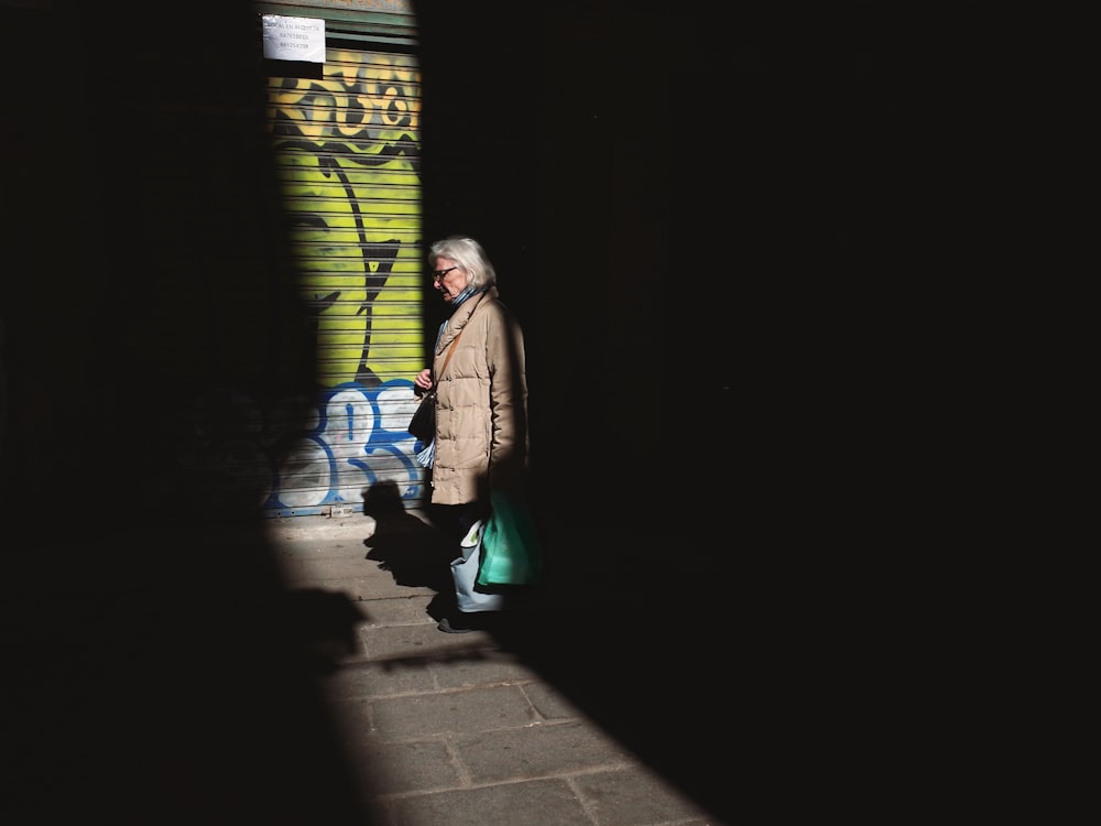 Frau in braunem Mantel und grüner Hose steht nachts auf dem Bürgersteig