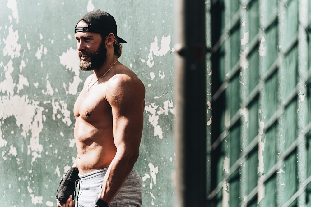 topless man in blue denim jeans standing beside blue wall during daytime