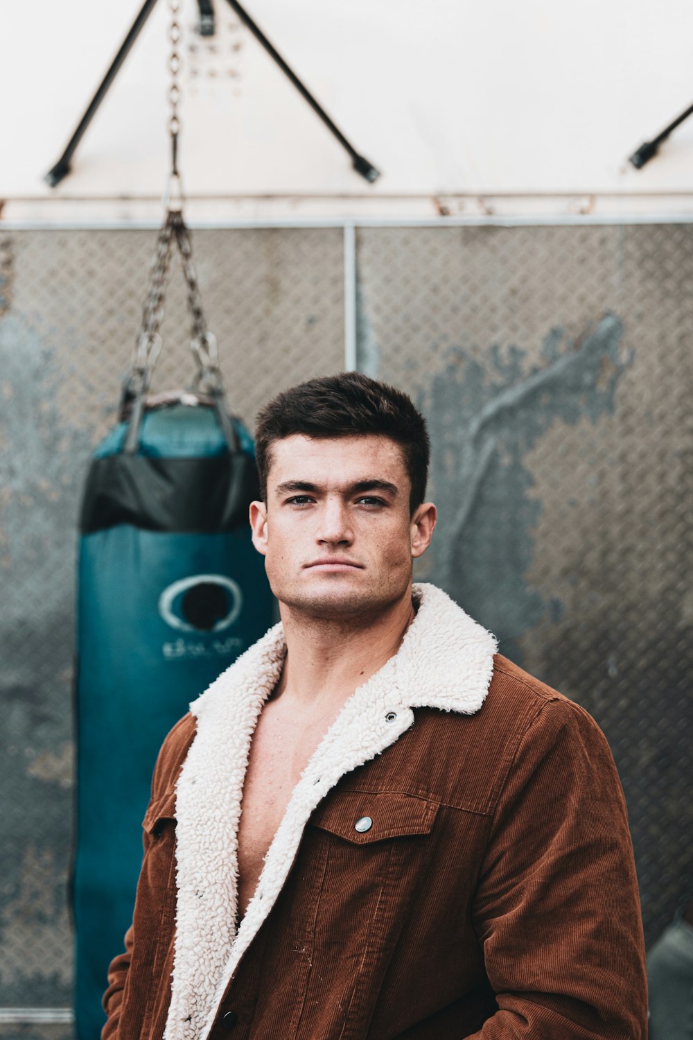 man in brown button up shirt standing beside blue and black heavy bag