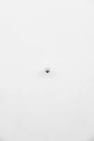A minimalist image featuring a single security camera mounted on a stark white wall. The camera is positioned slightly off-center towards the bottom of the frame, with its small, round shape creating a subtle focal point against the expansive white background.