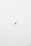 A minimalist image featuring a single security camera mounted on a stark white wall. The camera is positioned slightly off-center towards the bottom of the frame, with its small, round shape creating a subtle focal point against the expansive white background.