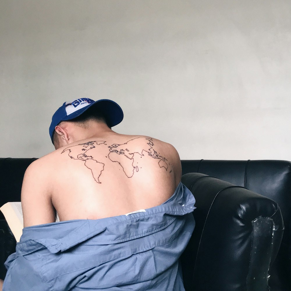 topless man wearing blue cap sitting on black leather couch