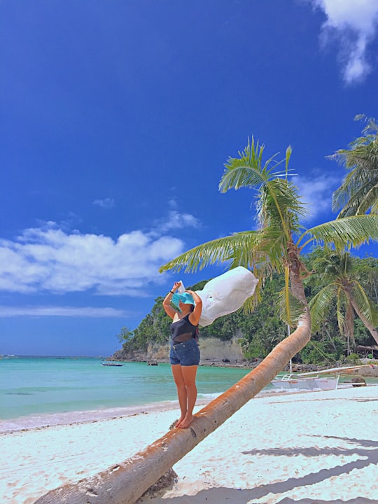 woman in blue denim shorts standing on beach shore holding white umbrella during daytime in Boracay Philippines