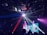 A lively club scene with a disco ball casting light beams across the room, creating a dynamic pattern of light and shadow. In the background, a colorful animated projection is displayed, adding to the vibrant atmosphere. Silhouettes of people are visible, enjoying the music and ambiance.