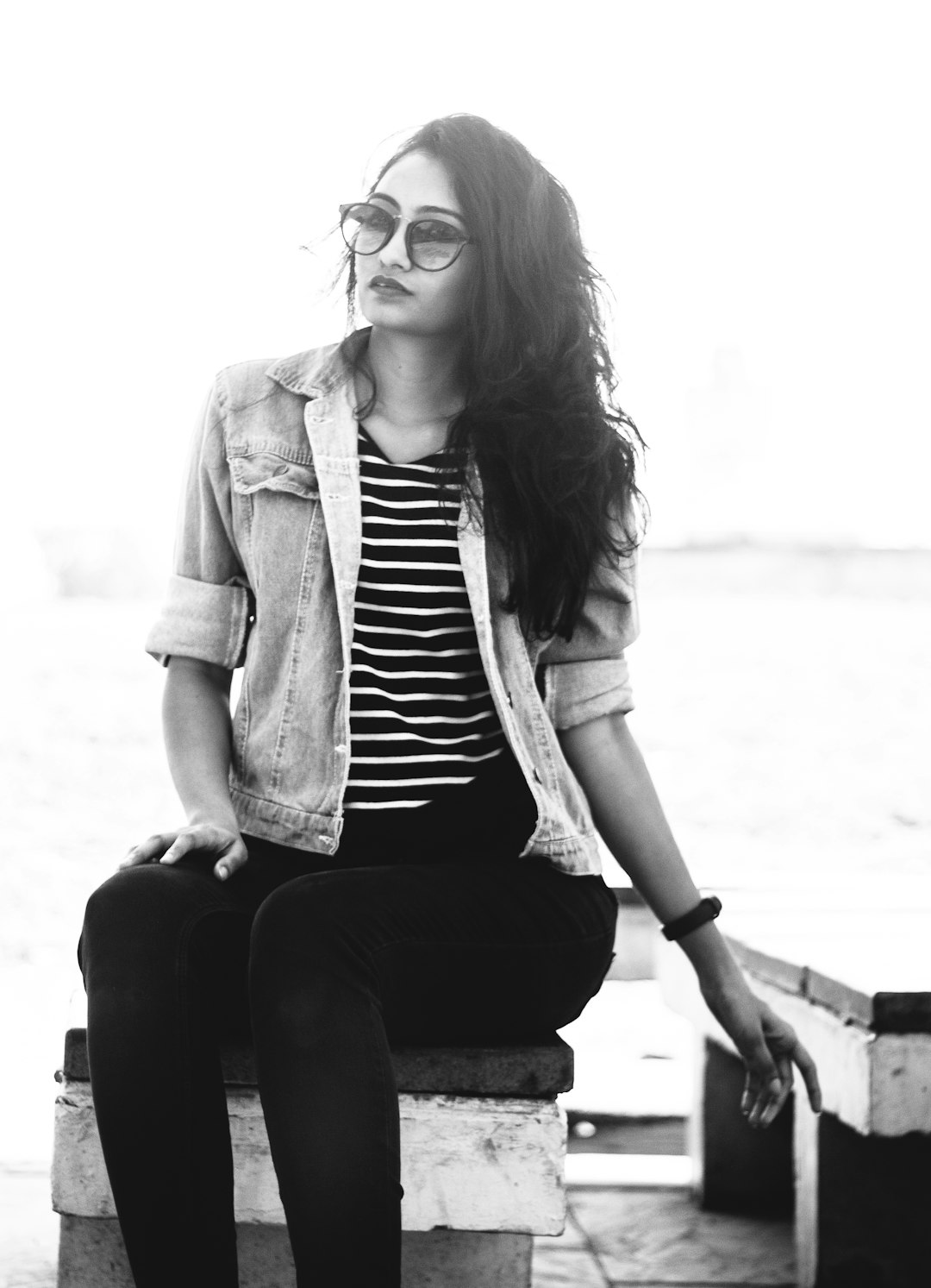 woman in black and white striped shirt and brown coat sitting on concrete bench