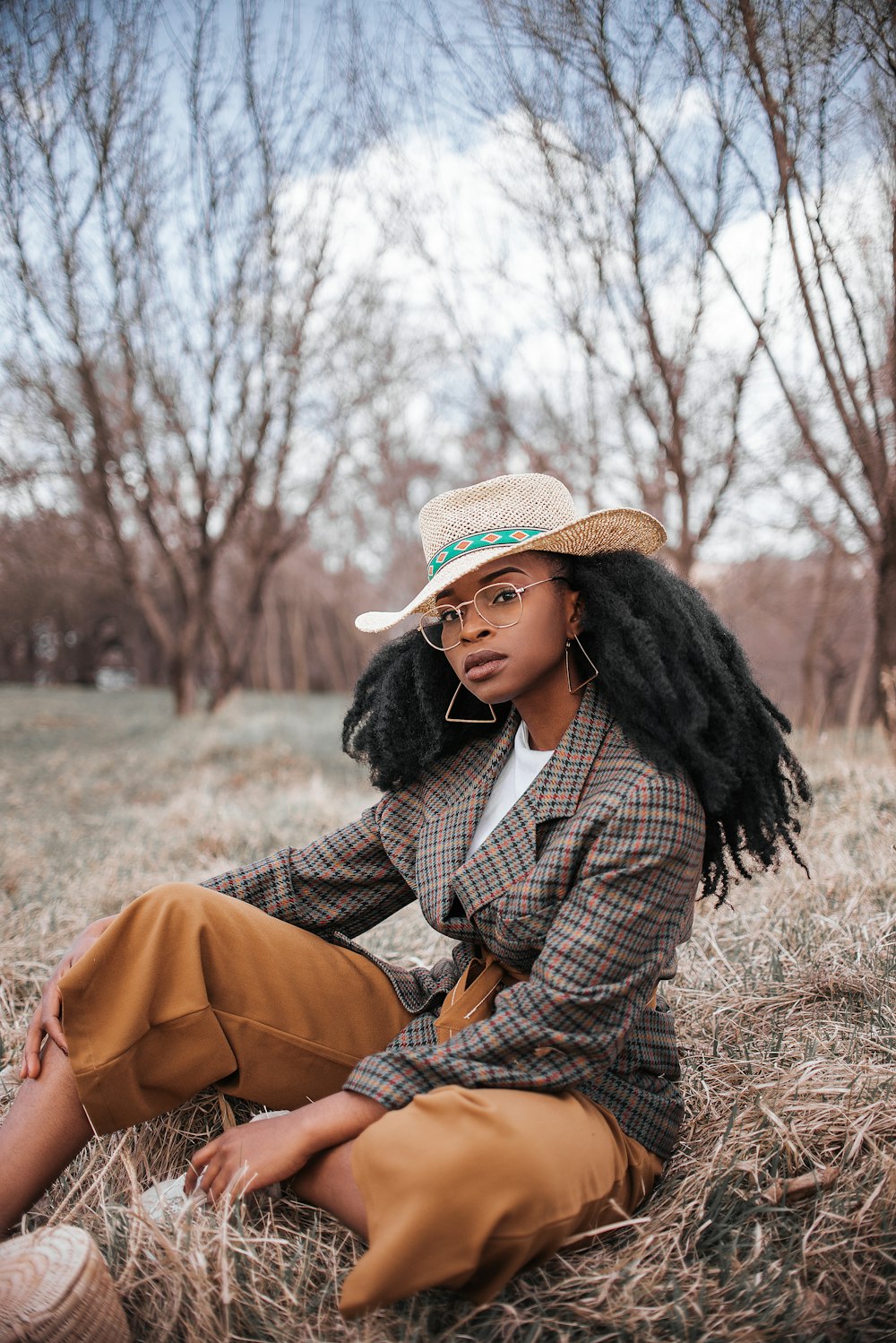 갈색 코트와 베이지색 모자를 쓴 여자가 낮 동안 갈색 잔디에 앉아 있다