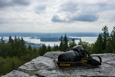 Perle Path camera bag resting on a rocky ledge overlooking a vast mountain landscape.