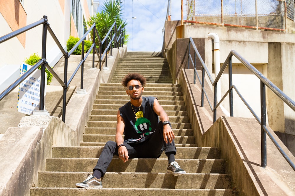 man in black and green crew neck t-shirt sitting on brown concrete stairs during daytime