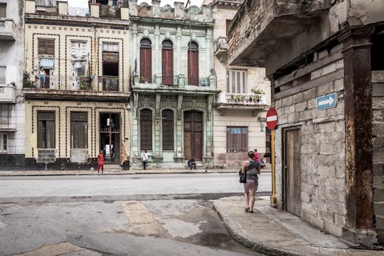 man in black jacket and blue denim jeans walking on sidewalk during daytime in Habana Cuba