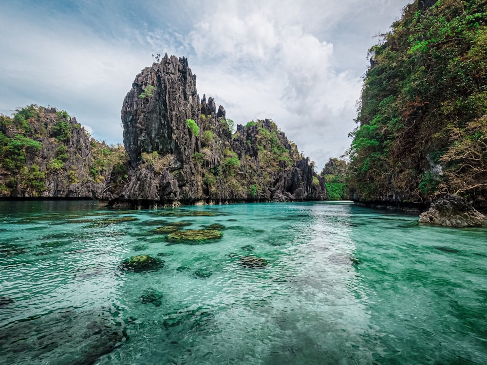 green and brown rock formation on blue sea under white clouds and blue sky during daytime