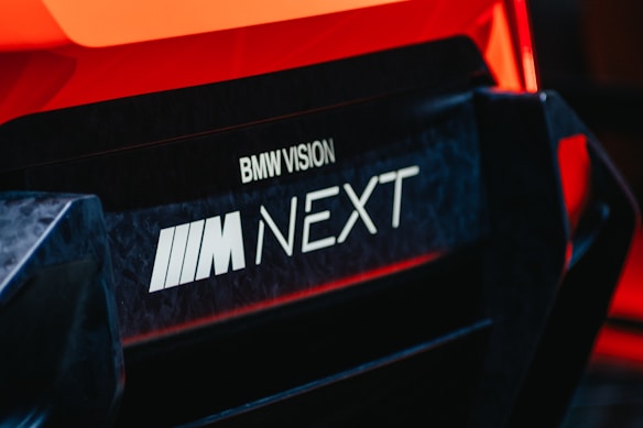 Close-up of a car with branding text 'BMW Vision M Next' prominently displayed. The image captures the sleek and modern design elements of the vehicle, emphasizing its futuristic aesthetic.