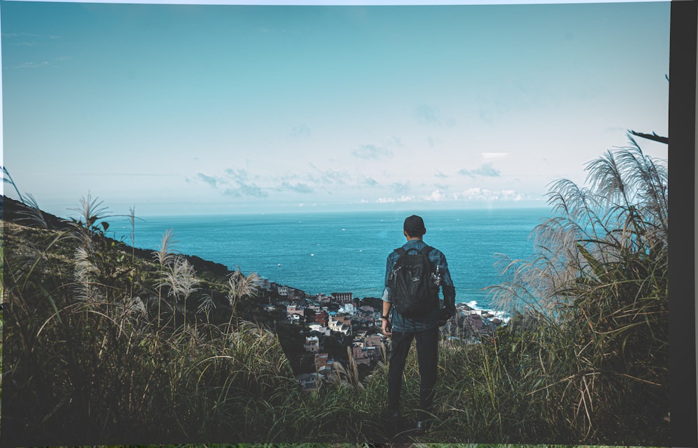 man in black jacket standing on cliff looking at the sea during daytime