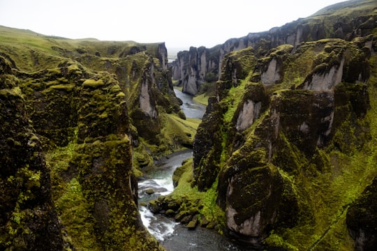 river between green and brown rocky mountain during daytime in Fjaðrárgljúfur Iceland