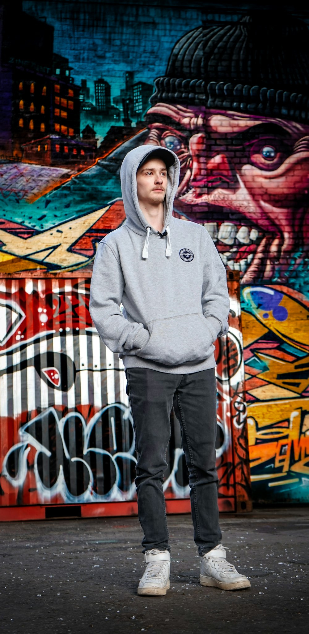 man in gray hoodie standing near graffiti wall