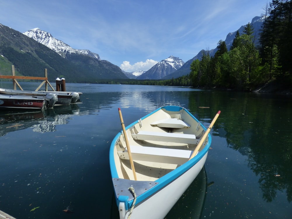 white and blue boat on water near green trees and mountain during daytime