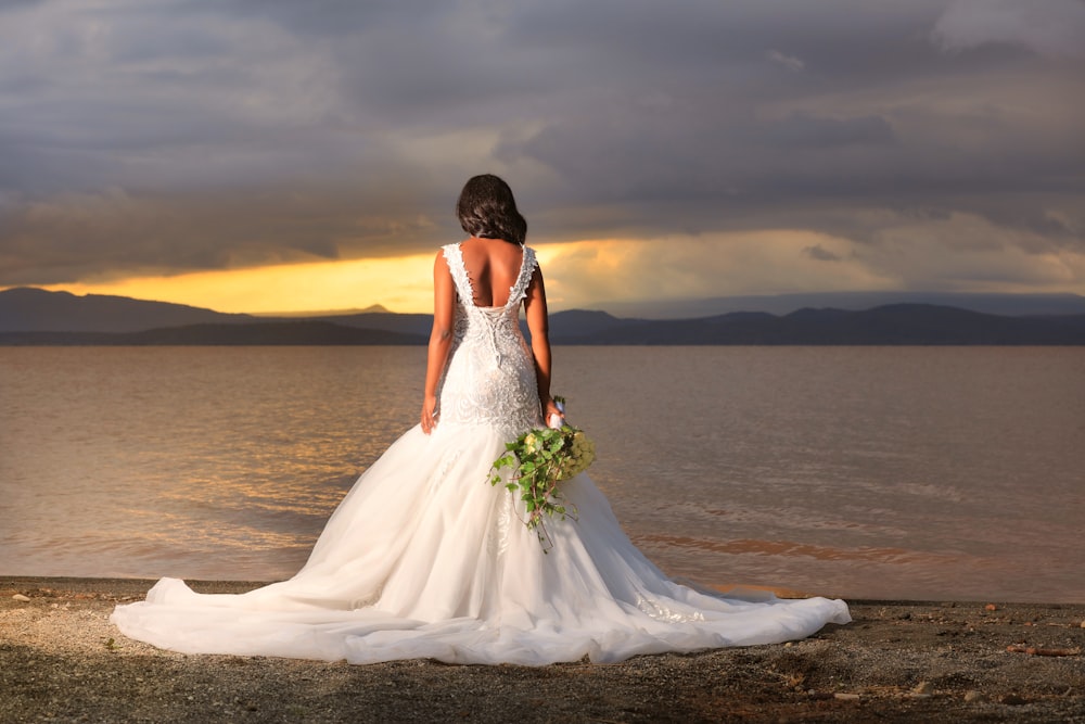 woman in white wedding dress standing on beach during sunset