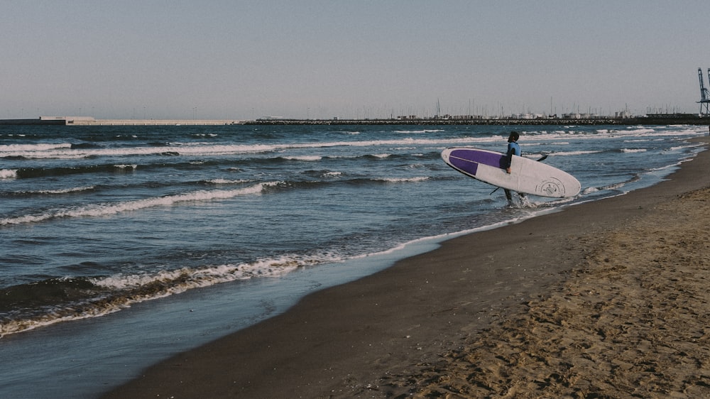 man in black shirt holding white and purple surfboard on beach during daytime