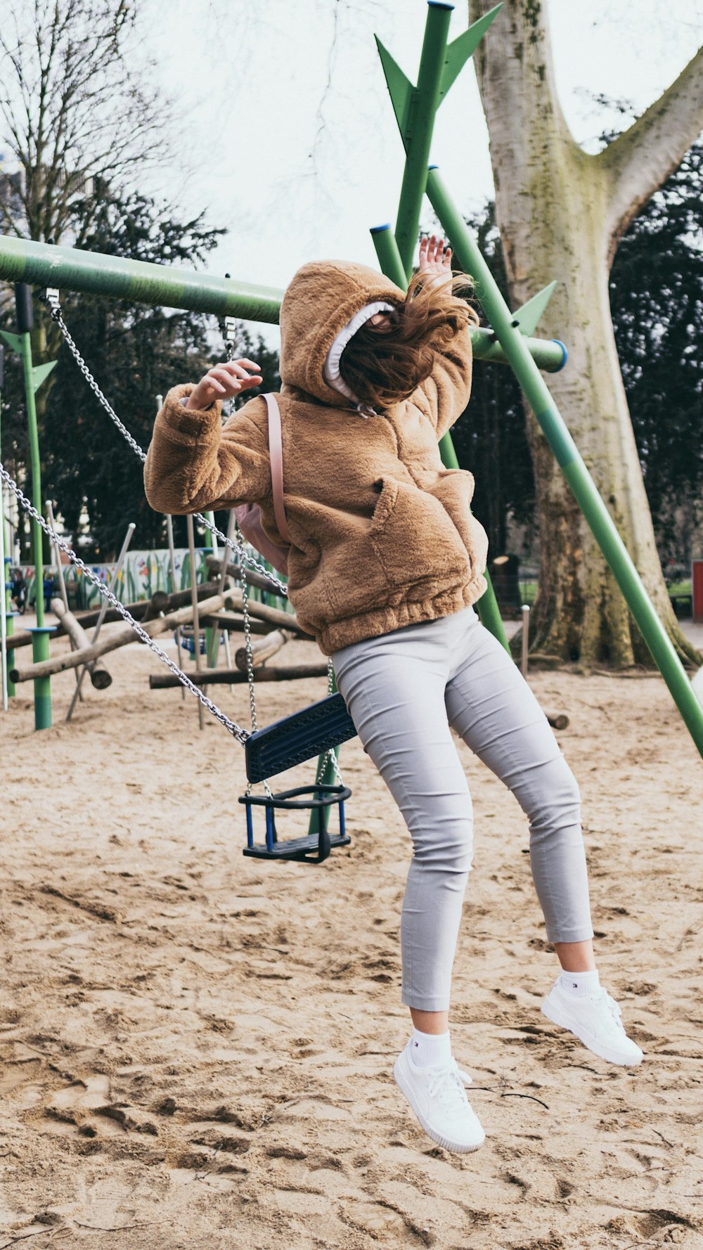 woman in brown jacket and white pants sitting on green metal bar during daytime