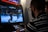 A person is playing a fighting video game on an arcade machine. The screen shows two characters engaged in a battle in a snowy setting. The person playing is focused, wearing glasses, and a striped shirt.