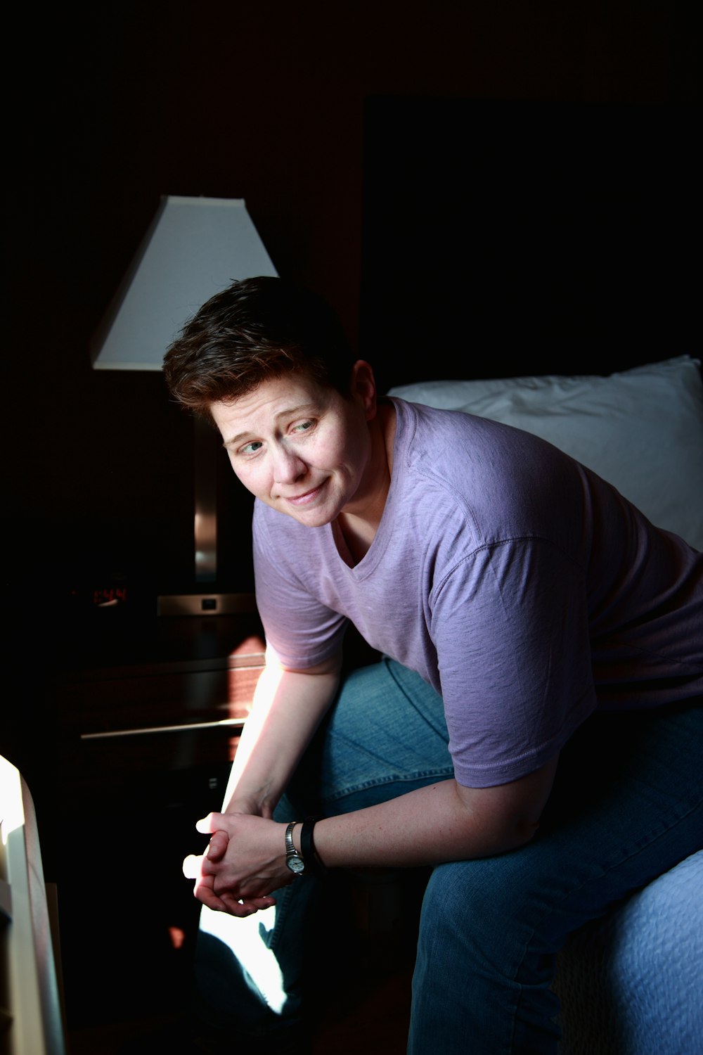 ベッドに座っているグレーのクルーネックTシャツの女性