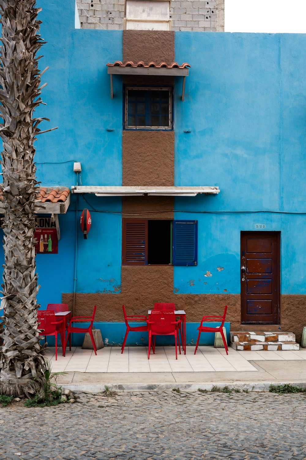 Sillas y mesas de plástico rojo cerca de un edificio de hormigón azul