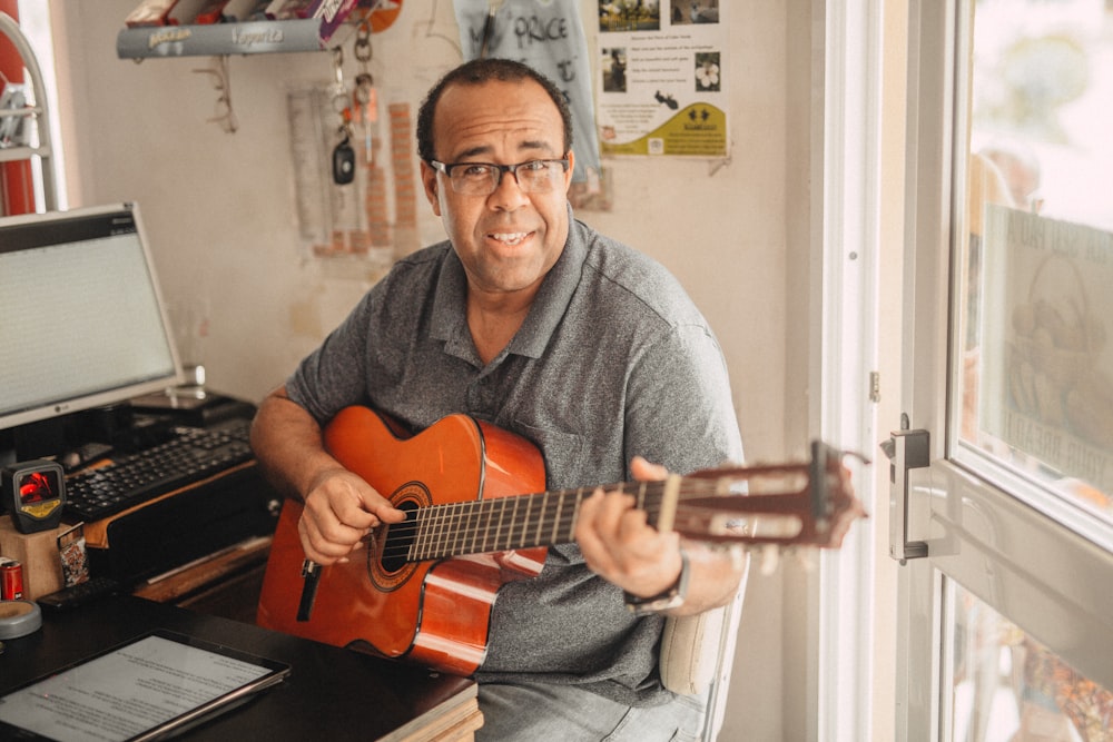 uomo in maglione grigio che suona la chitarra acustica marrone