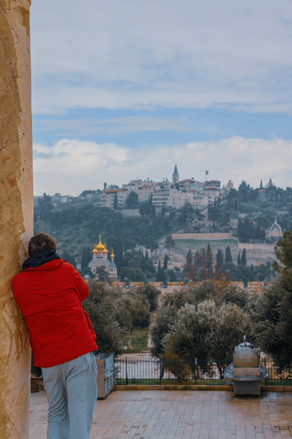 person in red hoodie sitting on brown concrete post looking at city during daytime