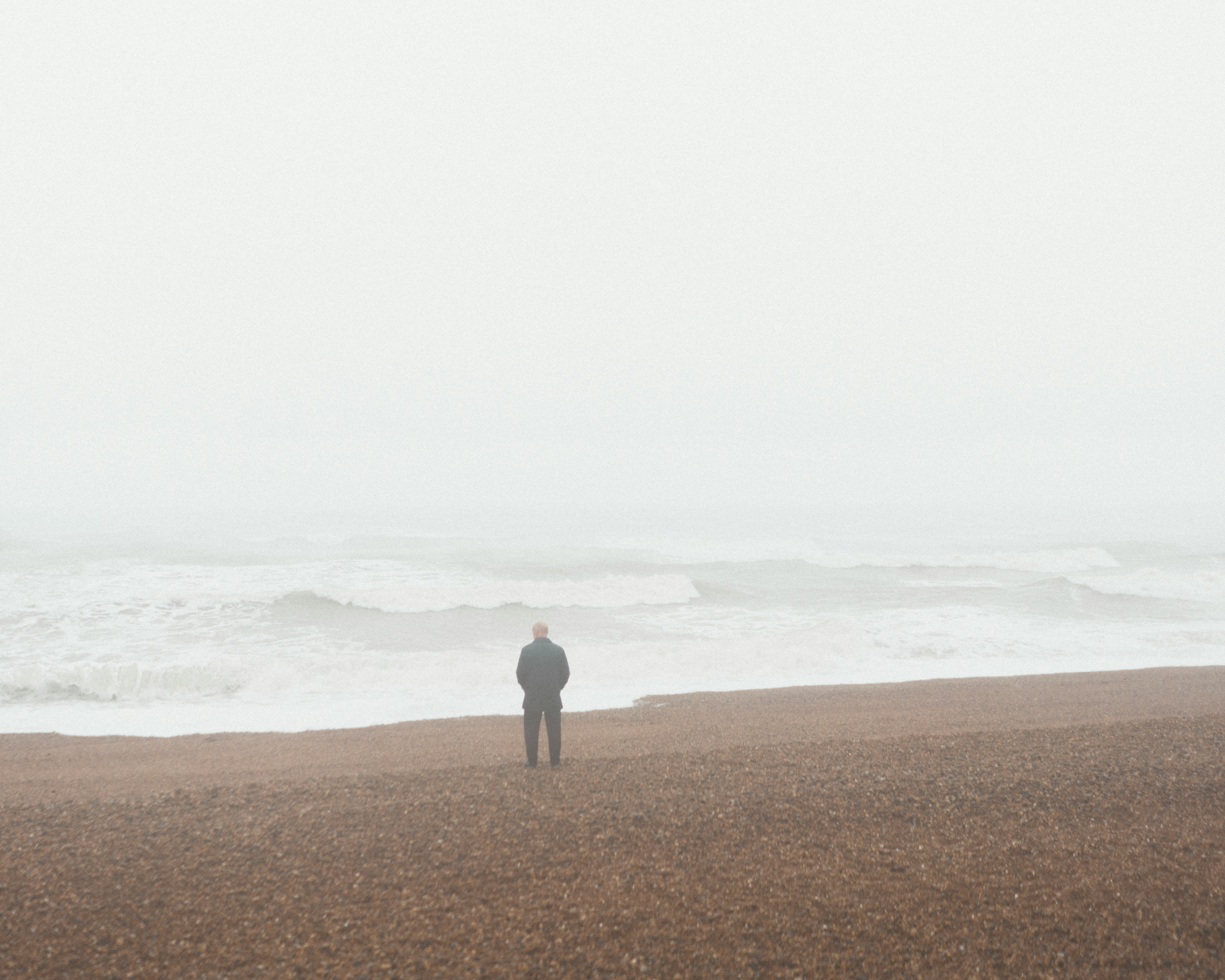 person in gray shirt standing on brown sand near sea during daytime