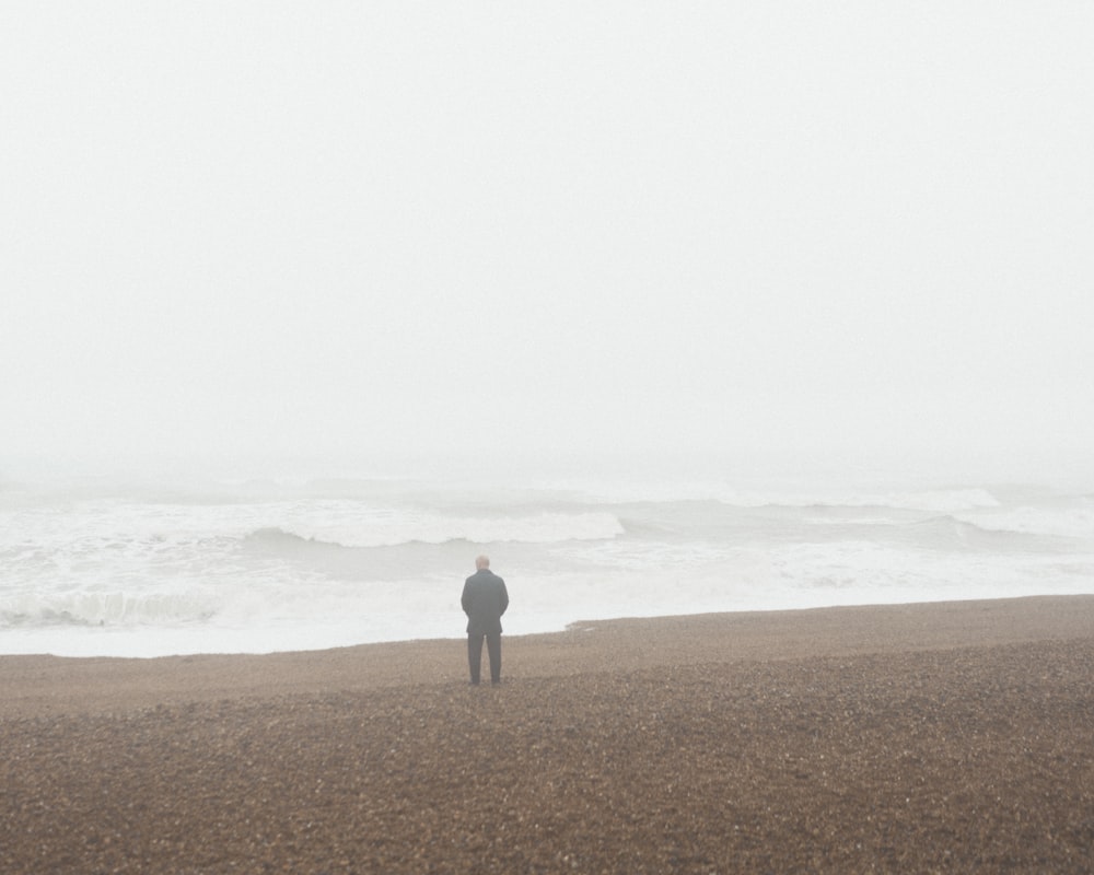 person in gray shirt standing on brown sand near sea during daytime