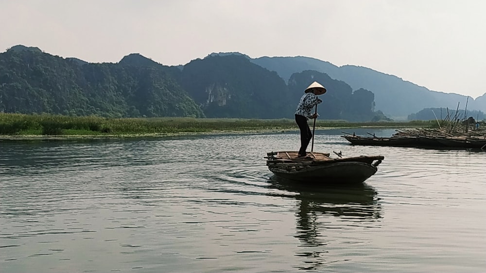 woman in white shirt and blue denim jeans standing on brown wooden boat on lake during