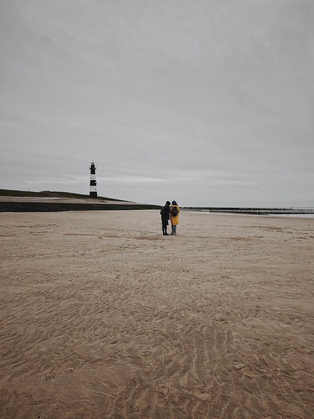 Mann in schwarzer Jacke steht tagsüber auf braunem Sand in der Nähe von Gewässern