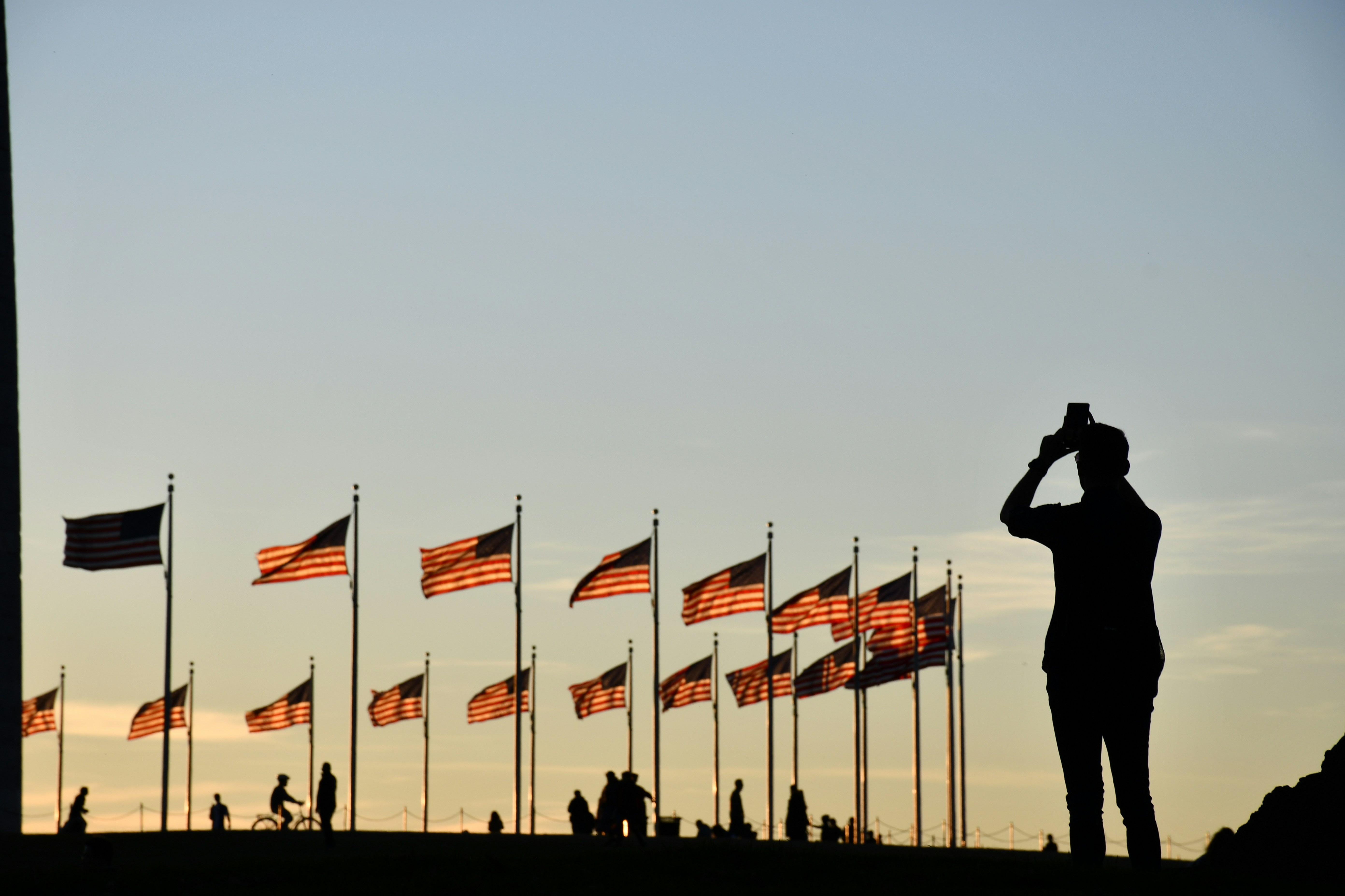 silhouette of man standing near flags during daytime washington monument teams background