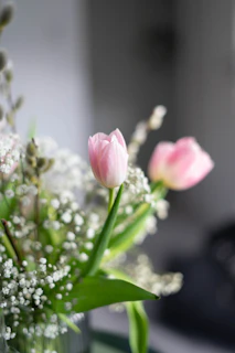 Close-up of a delicate arrangement combining white lilies with soft pink tulips on a light pastel background.