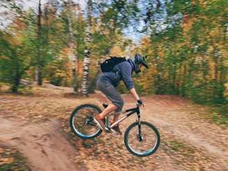 An adventurous cyclist carrying a sleek Amsonyns LLC backpack on a dirt trail surrounded by autumn leaves