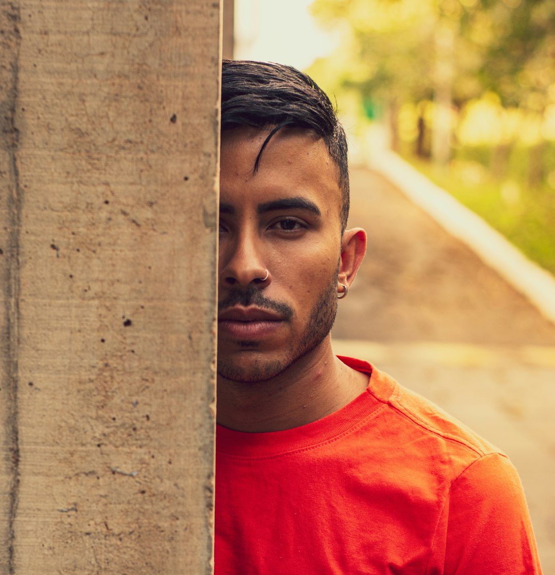 man in red crew neck shirt leaning on brown wooden post during daytime