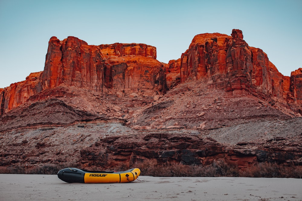 yellow and blue kayak on seashore near brown rock formation during daytime